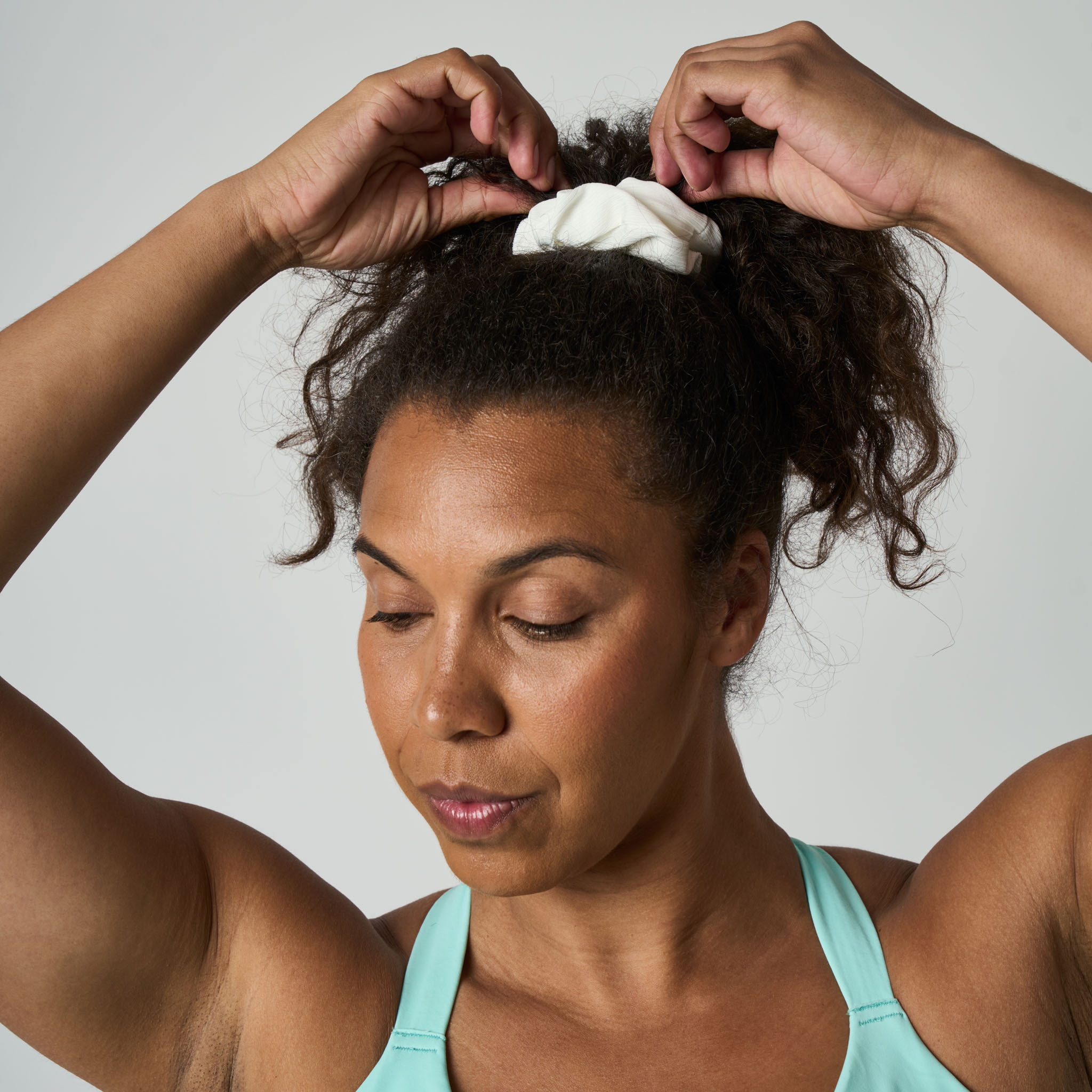 Woman adjusting a white hair tie in her hair against a neutral background