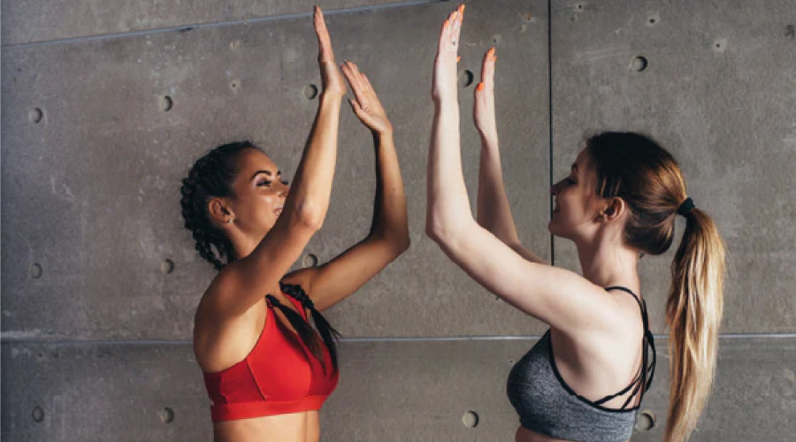 Two women High-five high ten in sports bras looking happy