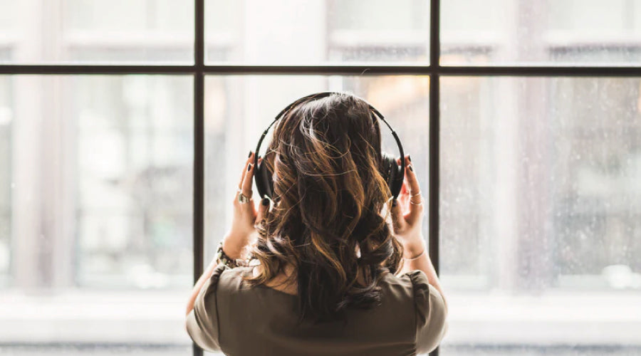 Brunette girl facing away, wearing headphones while looking out the window