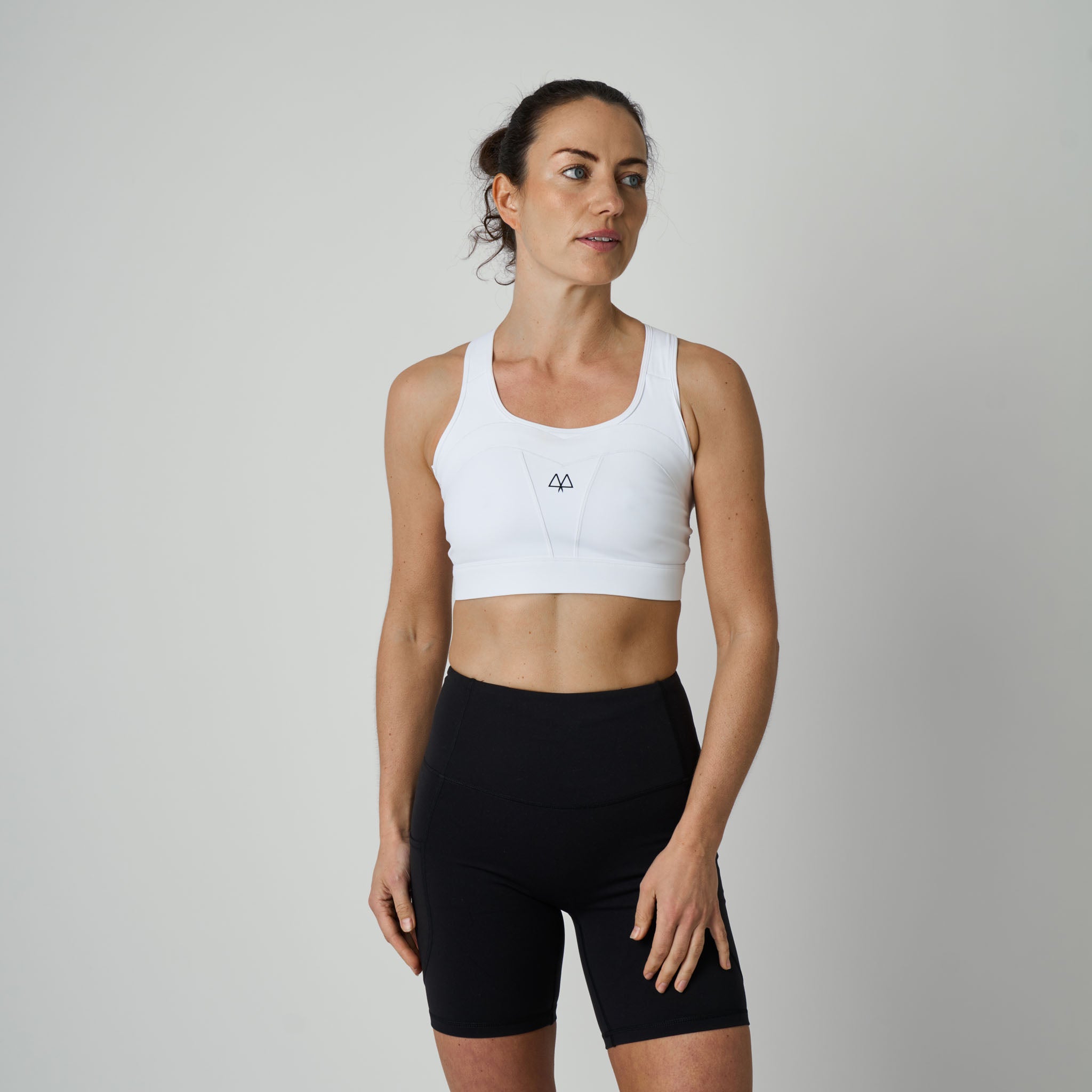 Woman wearing a white sports bra and black shorts on a plain background