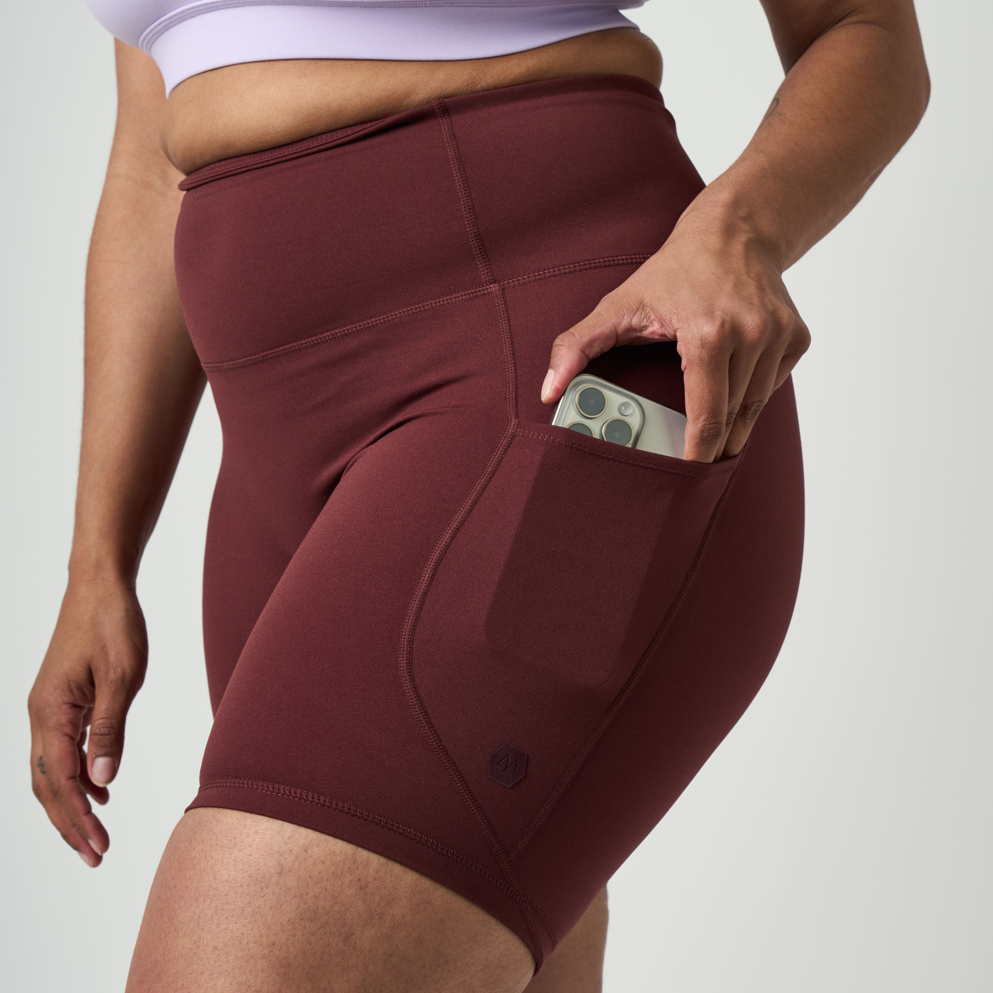 Maroon athletic shorts with a pocket held by a person on a light gray background