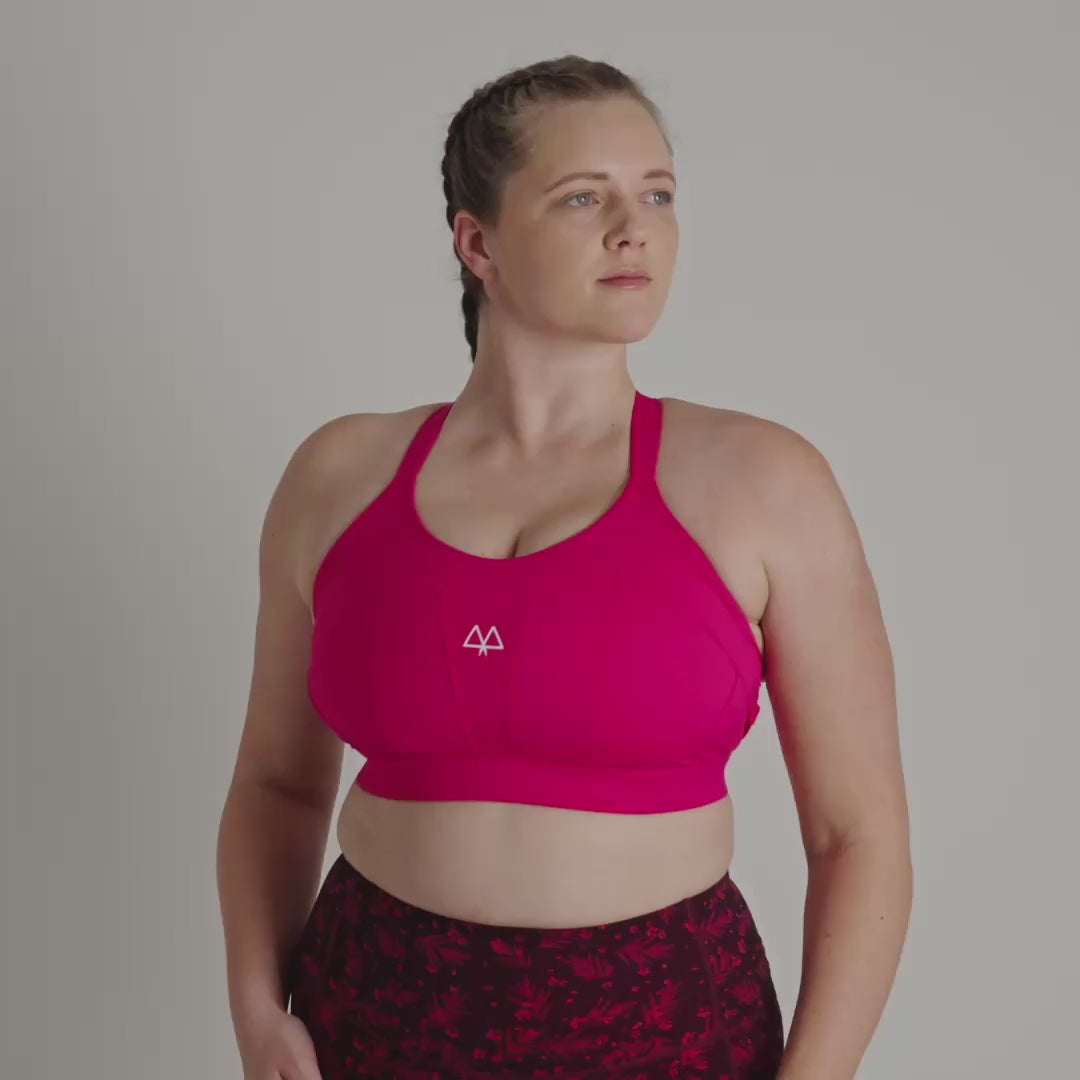 Woman wearing a pink sports bra and maroon patterned leggings on a gray background