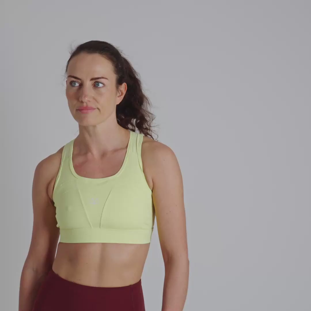 Woman wearing a yellow sports bra with a visible brand logo on a plain background