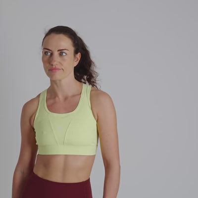 Woman wearing a yellow sports bra with a visible brand logo on a plain background